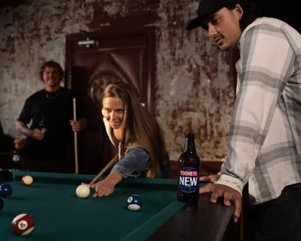 Friends playing pool enjoying a Tooheys New longneck